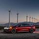 A photo of a red Mercedes EQS Sedan parked in a wind farm.
